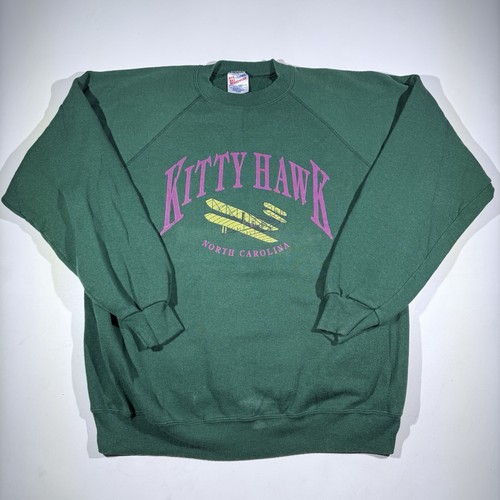 Green vintage Hanes Kitty Hawk sweatshirt with purple “Kitty Hawk North Carolina” text and surfboard graphic on front.