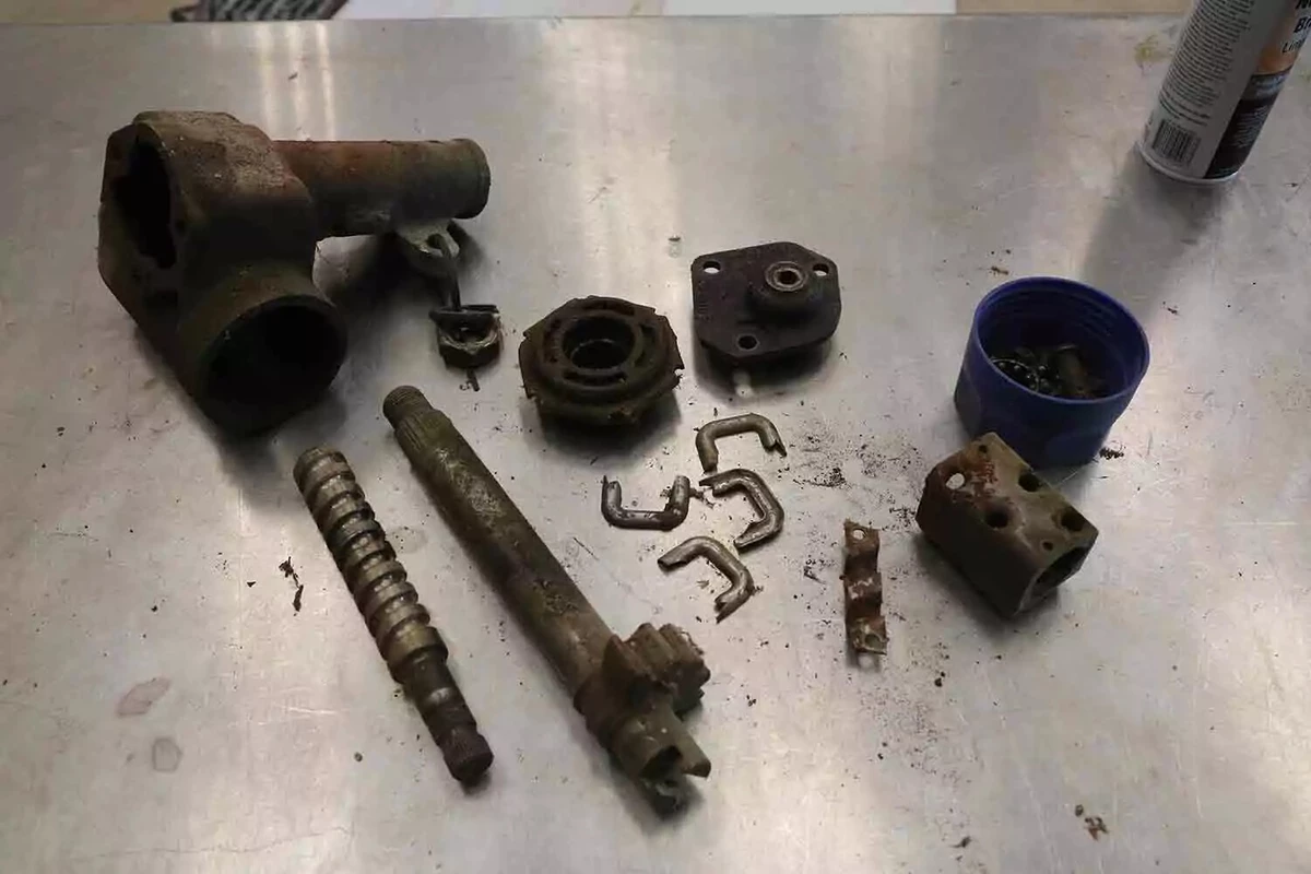 A disassembled old steering box’s components, displayed on a metal work surface.