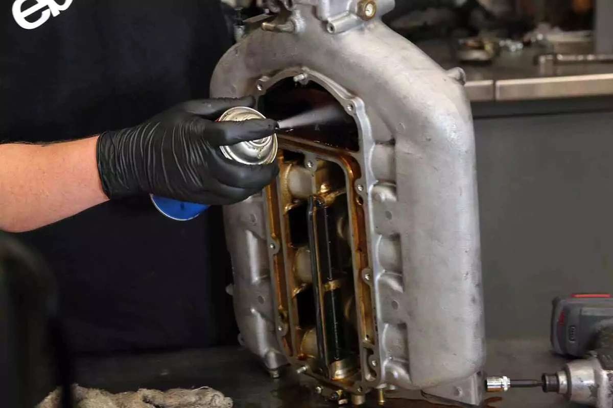 A mechanic sprays the inside of the intake manifold with throttle-body cleaner to remove varnish and residue.