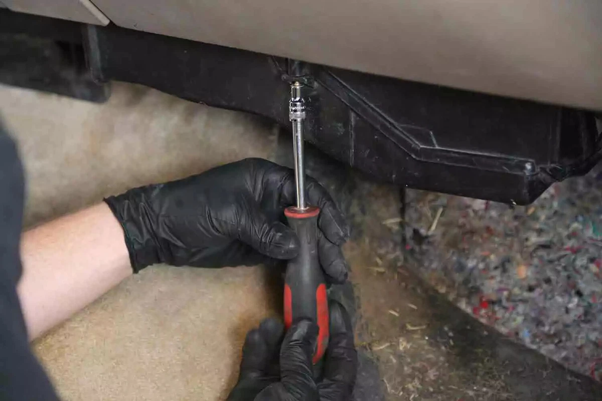 A mechanic wearing black gloves tightens the fasteners on the HVAC box cover.