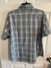 Men’s long-sleeve button-up shirt with green, purple, and yellow plaid pattern, displayed on a hanger against a white door.