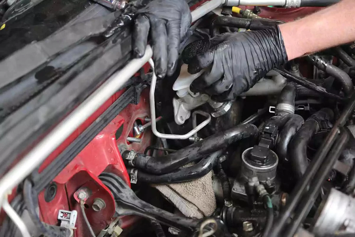 A mechanic wearing black gloves installs a new clutch master into the firewall.