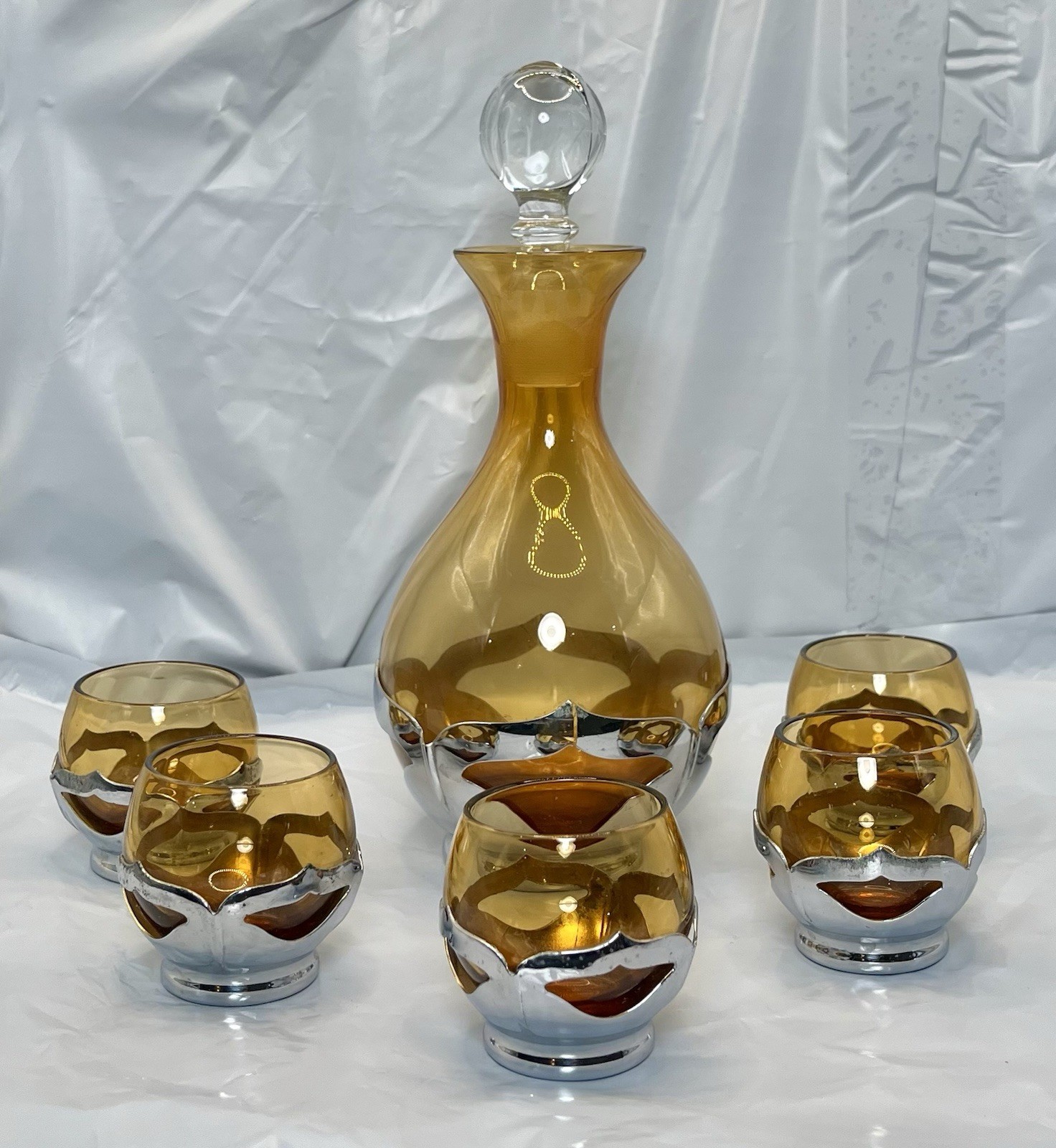 Amber glass decanter and shot glasses in a chrome Krome Kraft holder on a white background.