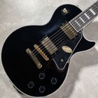 Black Epiphone LP Custom electric guitar with gold hardware, silver fret markers, and branded control knobs on a light background.