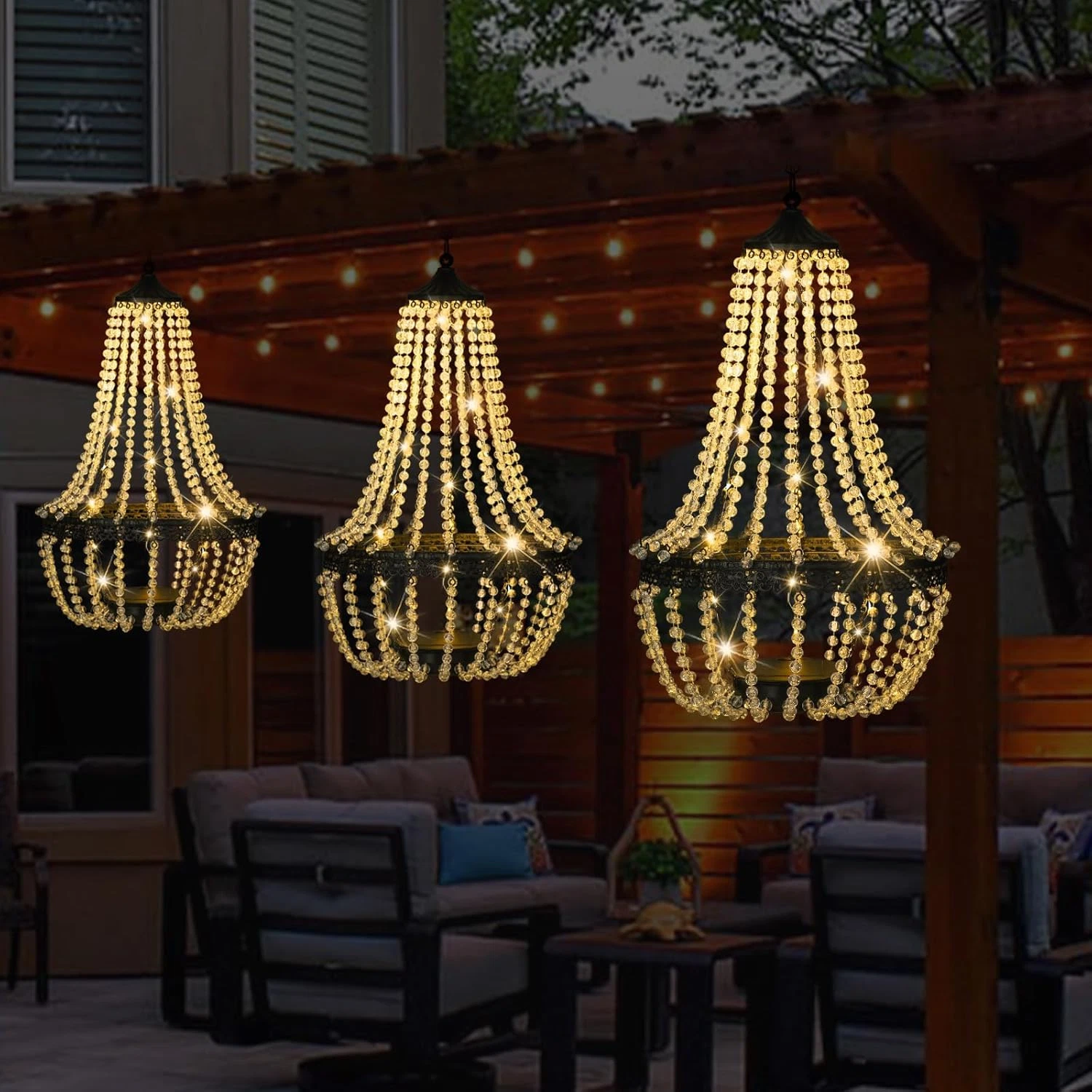 Three LumeVine solar chandeliers hanging over an outdoor patio seating area at night