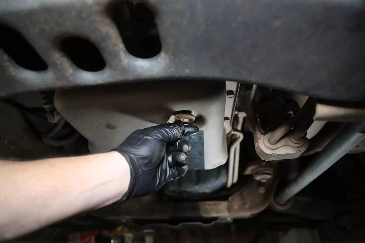 A mechanic unthreads and removes the automatic transmission drain plug.