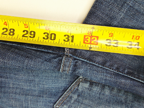 Yellow measuring tape with black vertical scale marked 28X31, placed on blue denim jeans with five-pocket design.