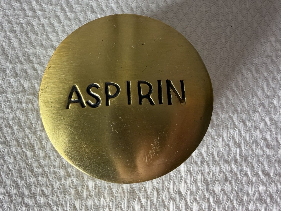 A solid brass paperweight shaped like a giant ASPIRIN pill — mid-century deadpan humor that hits differently on a modern desk.