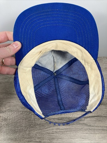 Blue Chicago Cubs snapback trucker hat with beige lining and mesh fabric, held against a wooden surface.
