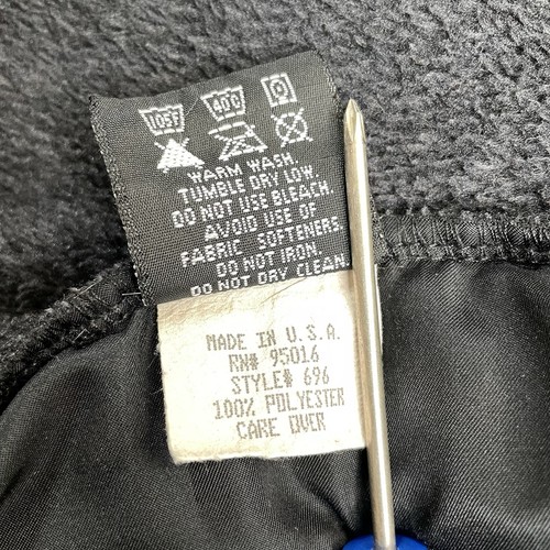 White fabric tag on black straight down vest, dark gray Polartec fleece, with iron, wash, and care instructions.