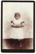 Fotografie Unglücklich blickender Knabe im Schürzenkleidchen 