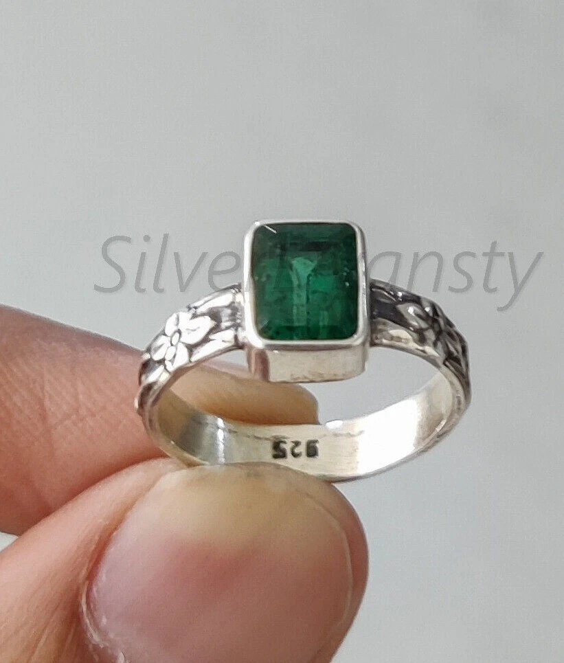 Lot - 89 An emerald, diamond and gold ring. The rectangular emerald cut in  steps and cut sides in a chaton is supported by two lines of...