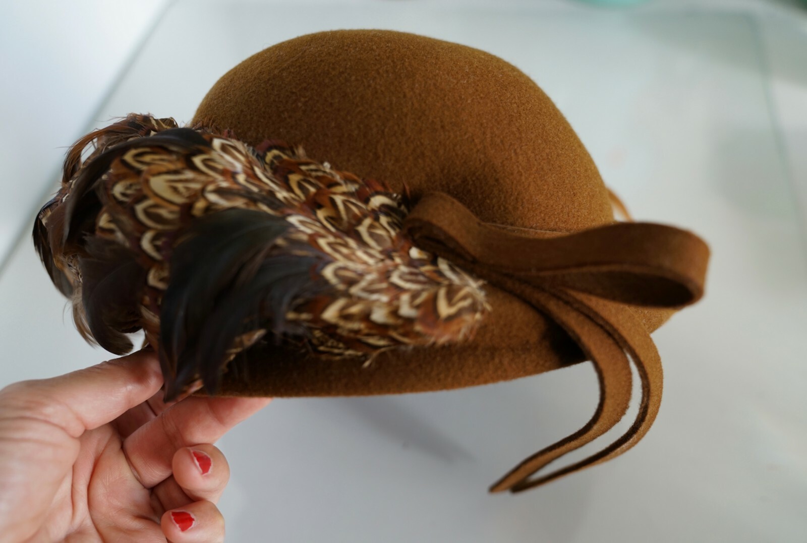Brown 100% wool hat with creased crown and tan ribbon, held in hand against white background.