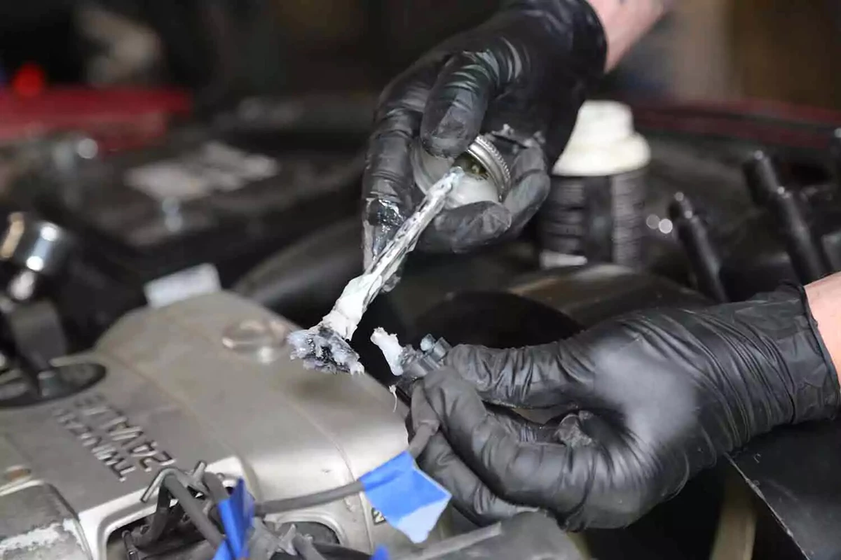 A mechanic wearing black gloves applies dielectric grease to a vehicle's plug wire boots.