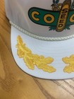 White vintage trucker hat with green brim, featuring yellow Coop Seed text and leaf graphics on the front panel.