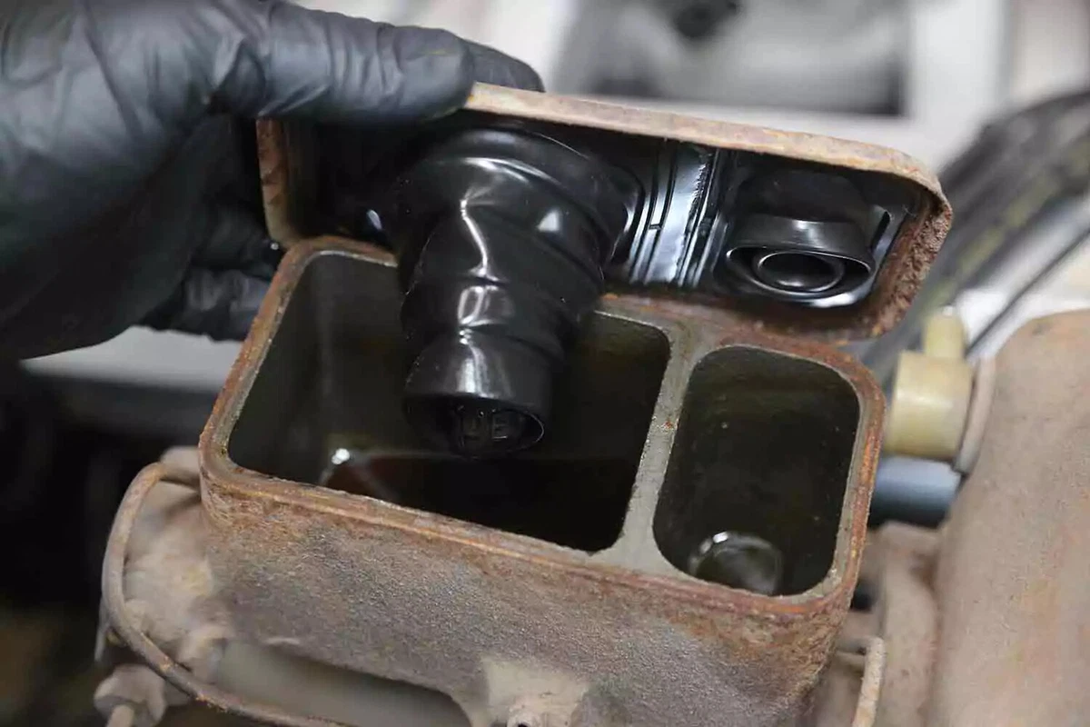 A mechanic wearing a black nitrile glove opens the lid on a brake master cylinder fluid reservoir. The fluid level is extremely low.