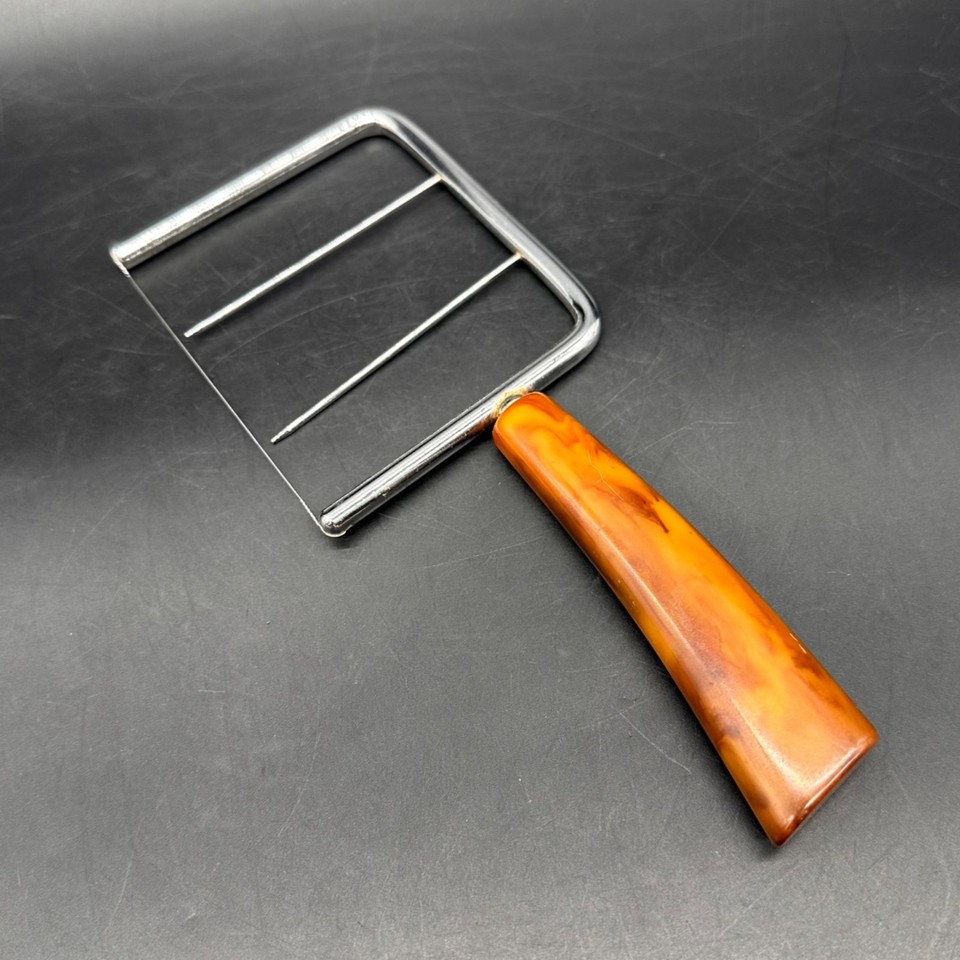 A butterscotch Bakelite-handled cheese slicer that looks like it belongs in a 1950s kitchen styled by a design museum — retro color, zero plastic junk energy.