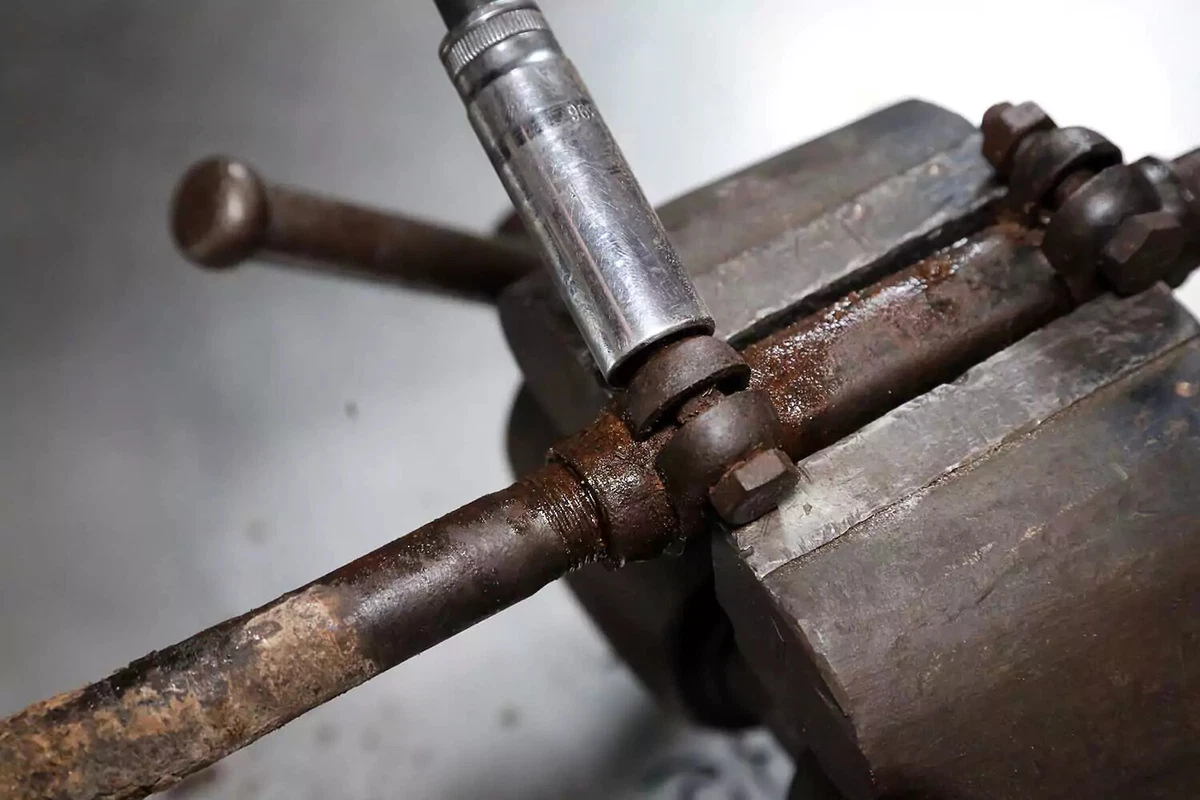 A mechanic loosens the tie rod end adjuster sleeve clamping bolt with a socket wrench.