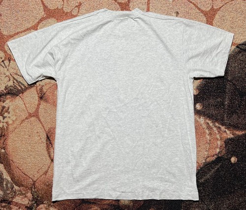 Gray single-stitch VINTAGE MADE IN USA T-shirt with back graphic, laid flat on a textured woven surface.