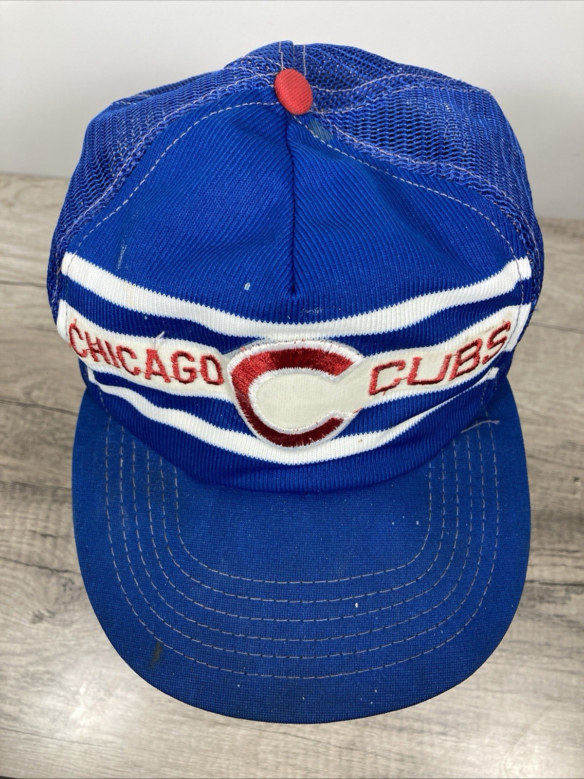 Blue snapback trucker hat with white and red stripe embroidery and a red button on the front panel.