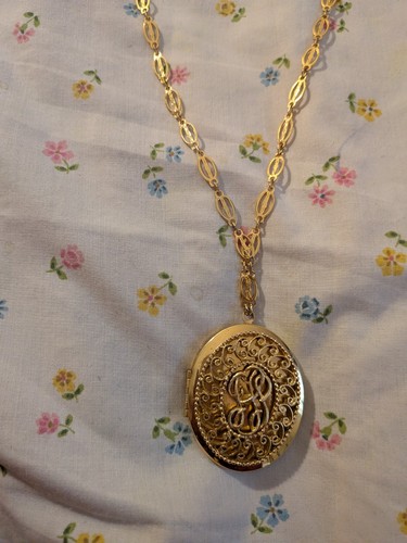This gold-tone necklace features an intricate, filigree-style oval locket.