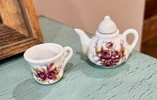 A miniature porcelain teapot and cup set with a red rose floral pattern.