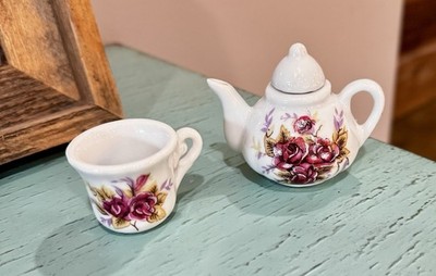 A miniature porcelain teapot and cup set with a red rose floral pattern.