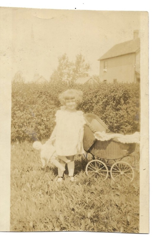 vintage photo girl holding antique doll by wicker carriage
