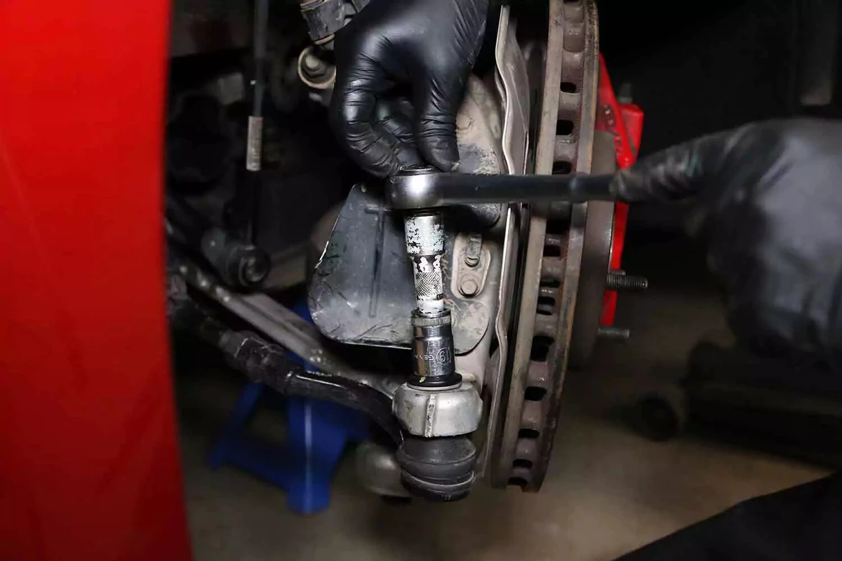 A mechanic uses a socket wrench to remove the castle nut from the tie rod end.