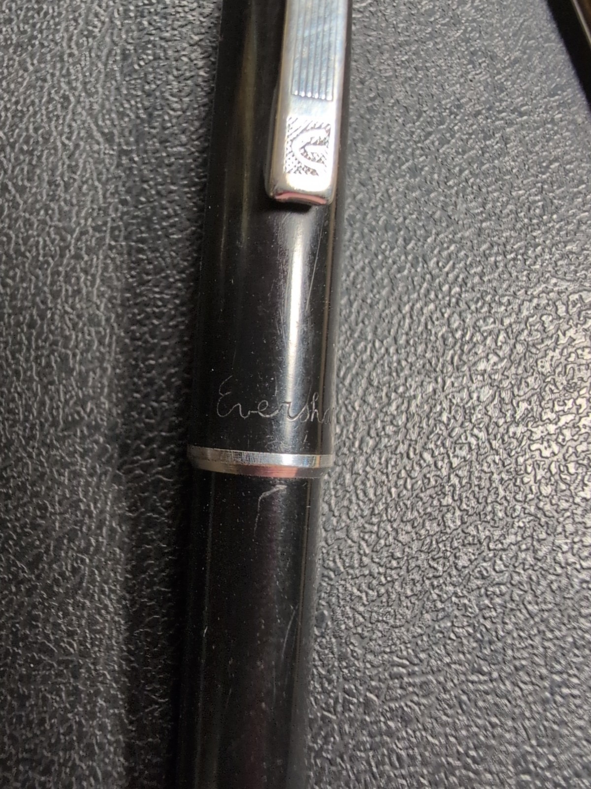 Black Eversharp mechanical pencil with silvertone trim, blue “Eversharp” text, and twist-out pen refills on a textured surface.