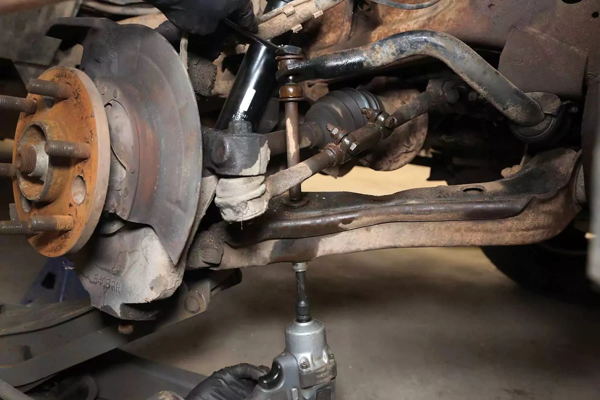 A mechanic removes the end link nut with an impact gun.