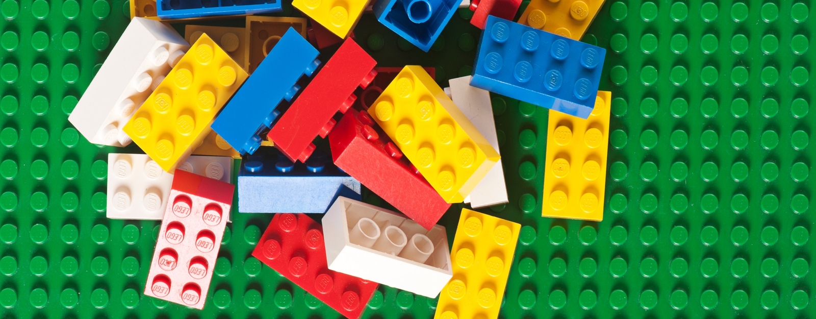 Aufnahme von verschiedenen bunten LEGO Steinen, die auf einer grünen Grundplatte willkürlich verteilt liegen.