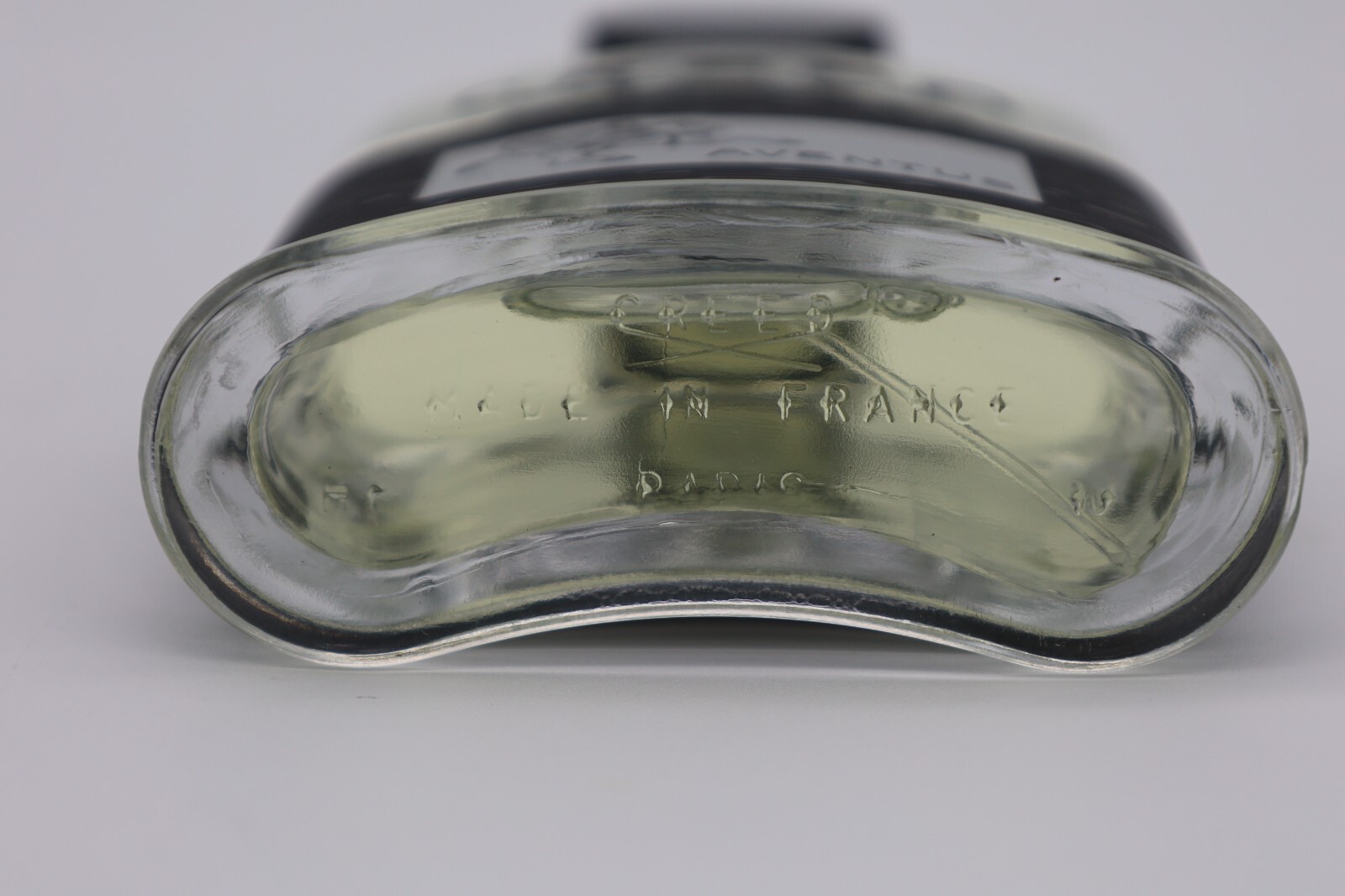 Clear glass bottle of Creed Aventus cologne, yellow liquid, black cap, text “Made in France” and “Dario” on base.