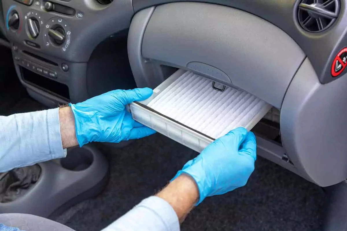 A mechanic wearing blue nitrile gloves inserts a brand new cabin air filter into place.