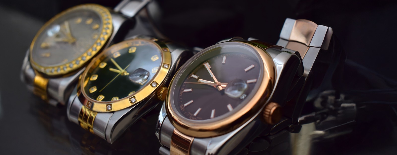 Drei stylische Armbanduhren mit unterschiedlichen Designs und Farben: Gold, Grün und Dunkelbraun, präsentiert auf einer dunklen Oberfläche.