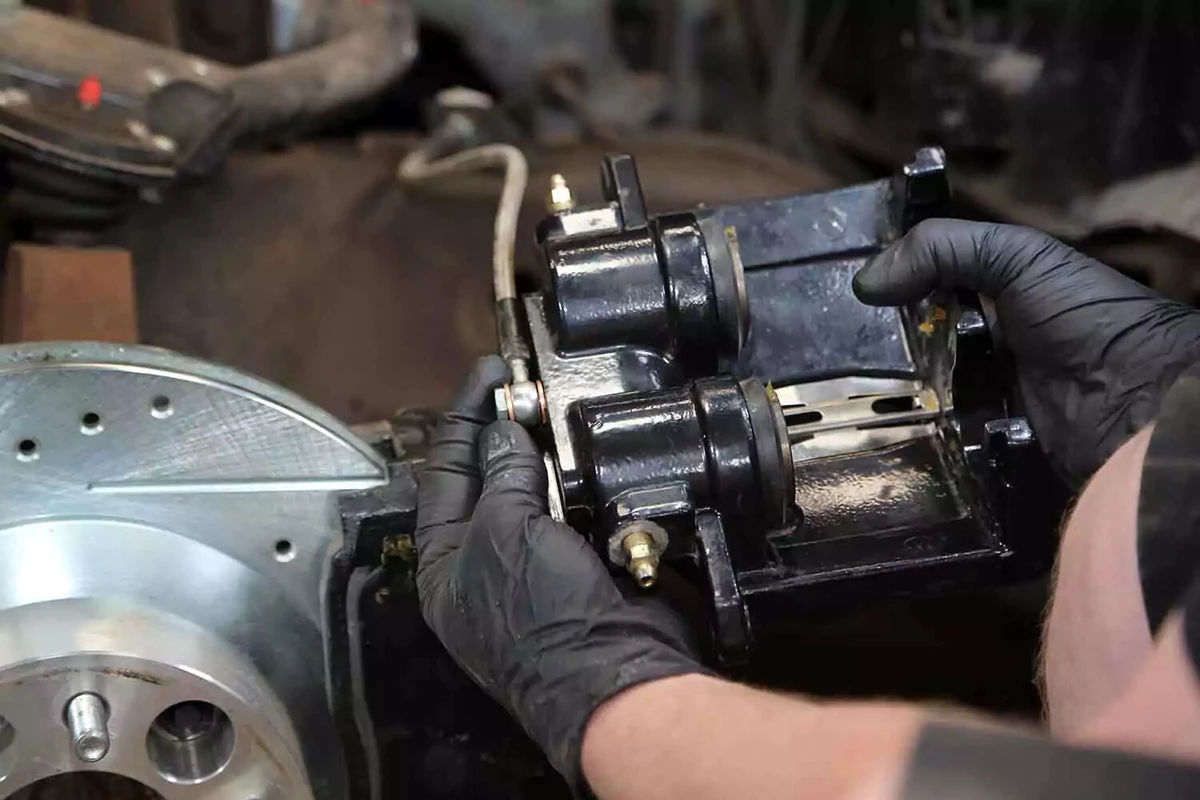A mechanic threads the brake line into the caliper by hand.