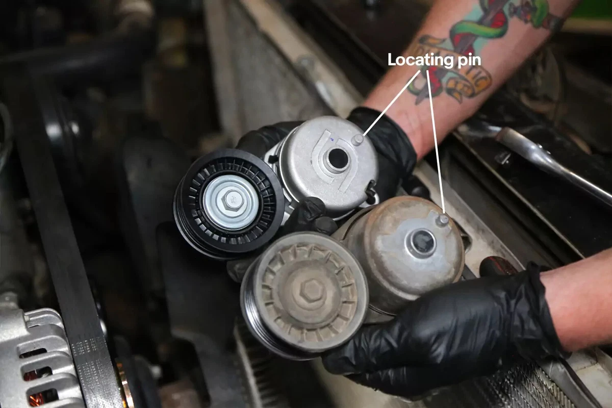 A mechanic wearing black glove compares new serpentine belts to the old ones.