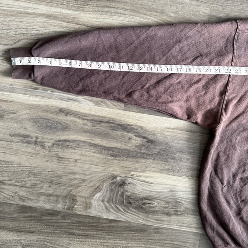 Brown vintage Nike sweatshirt with white swoosh, faded crewneck, and long sleeves, shown on wooden floor.