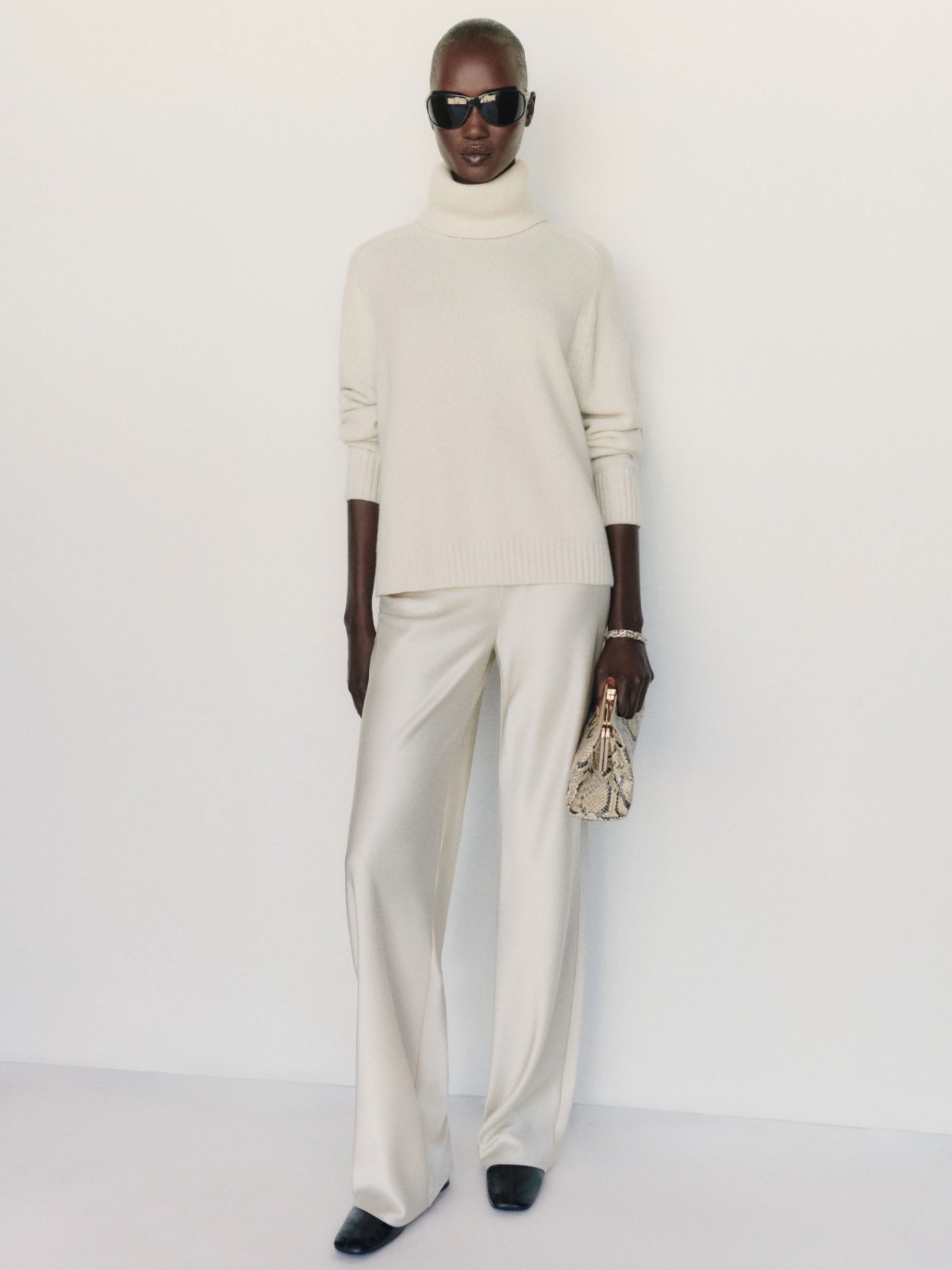 Woman wearing an ivory oversized cashmere turtleneck sweater with cream trousers.