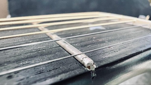Close-up of black Martin D-76 guitar with silver hardware and three straight guitar strings on a dark wood fretboard.
