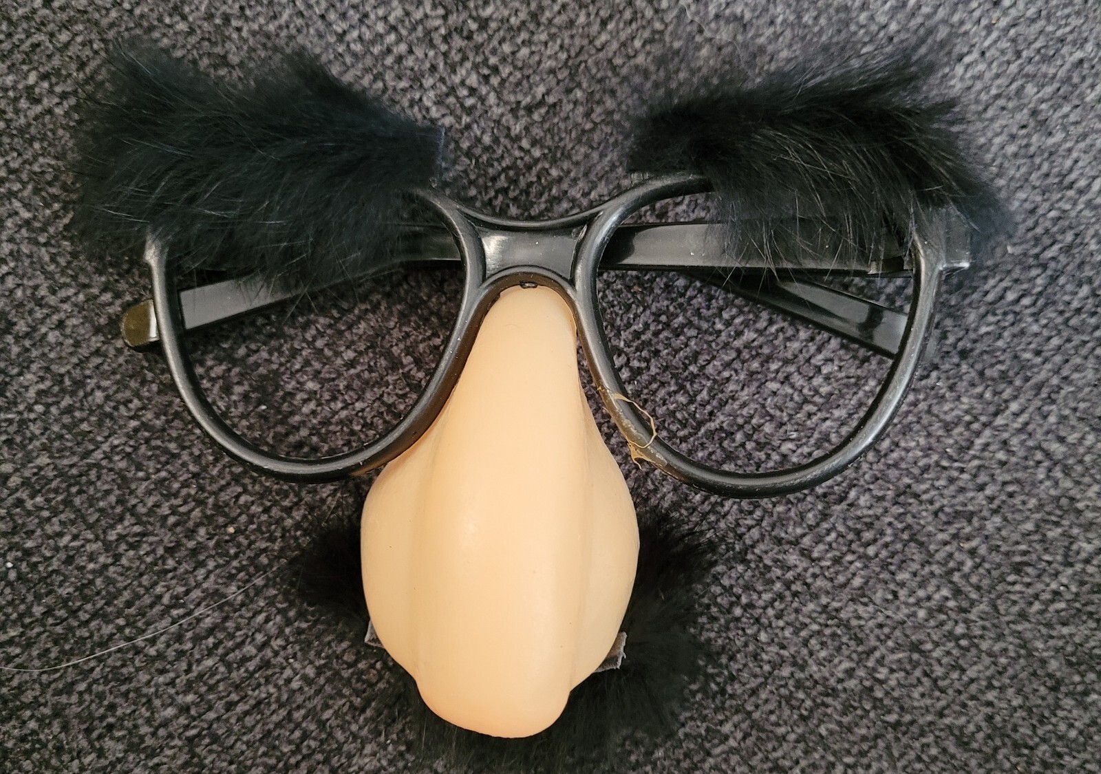Black and white novelty eyeglasses with large nose piece, small black ears, and clear lenses on a dark textured surface.