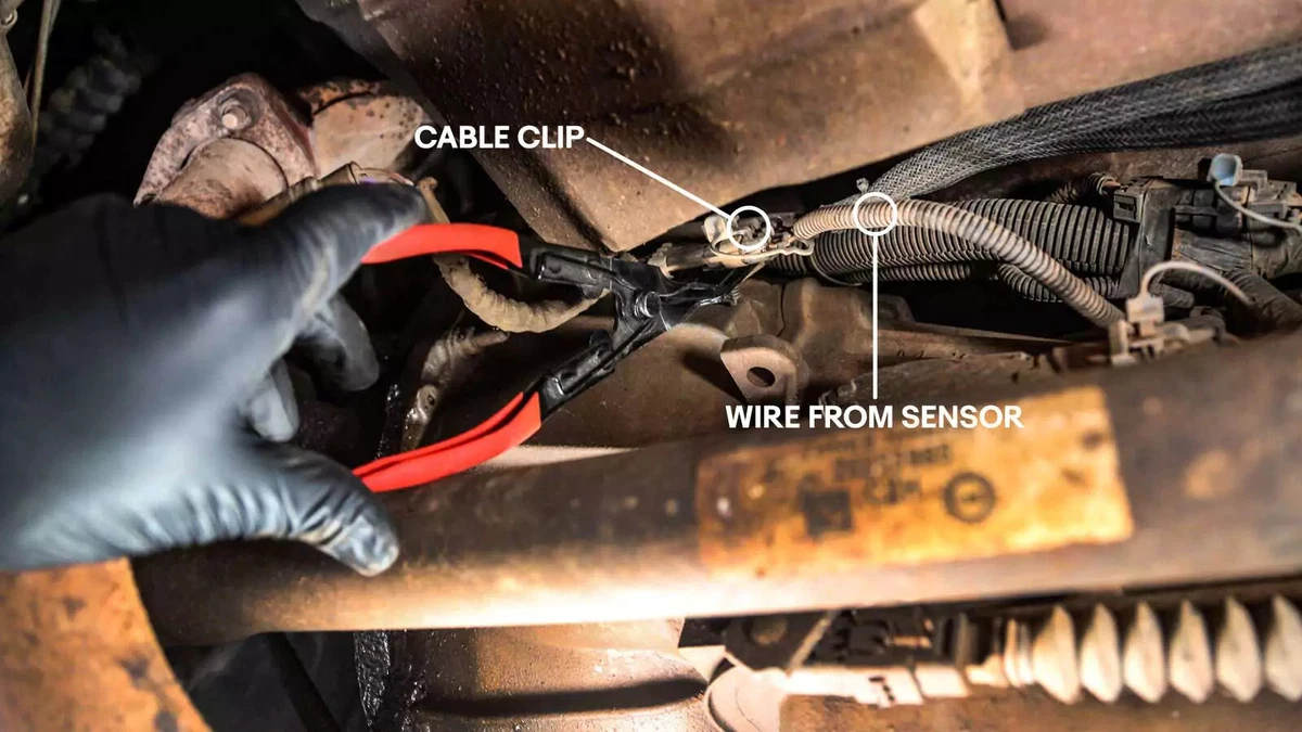 A mechanic using a pair of clip poppers to release the oxygen sensor’s plug.