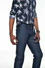 Man wearing navy blue denim men’s bootcut jeans with gold stitching, palm tree shirt, and black watch.