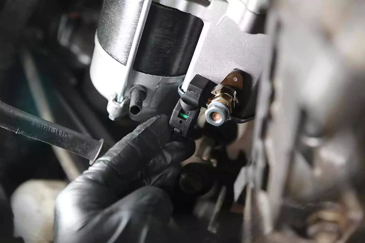 A mechanic wearing a black nitrile glove reconnects the trigger wire after replacing a starter.