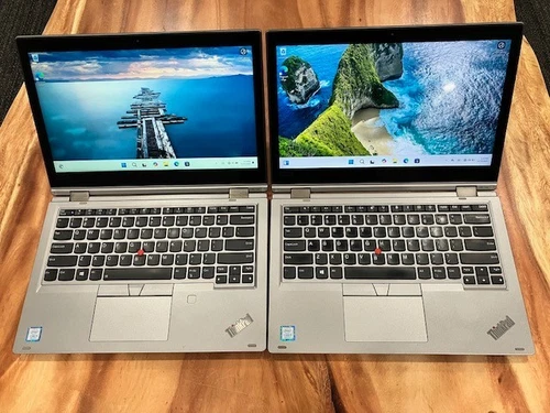 Two silver Lenovo Yoga L380 i5-8250 laptops with black touchscreens displaying mountain and coastal scenery.