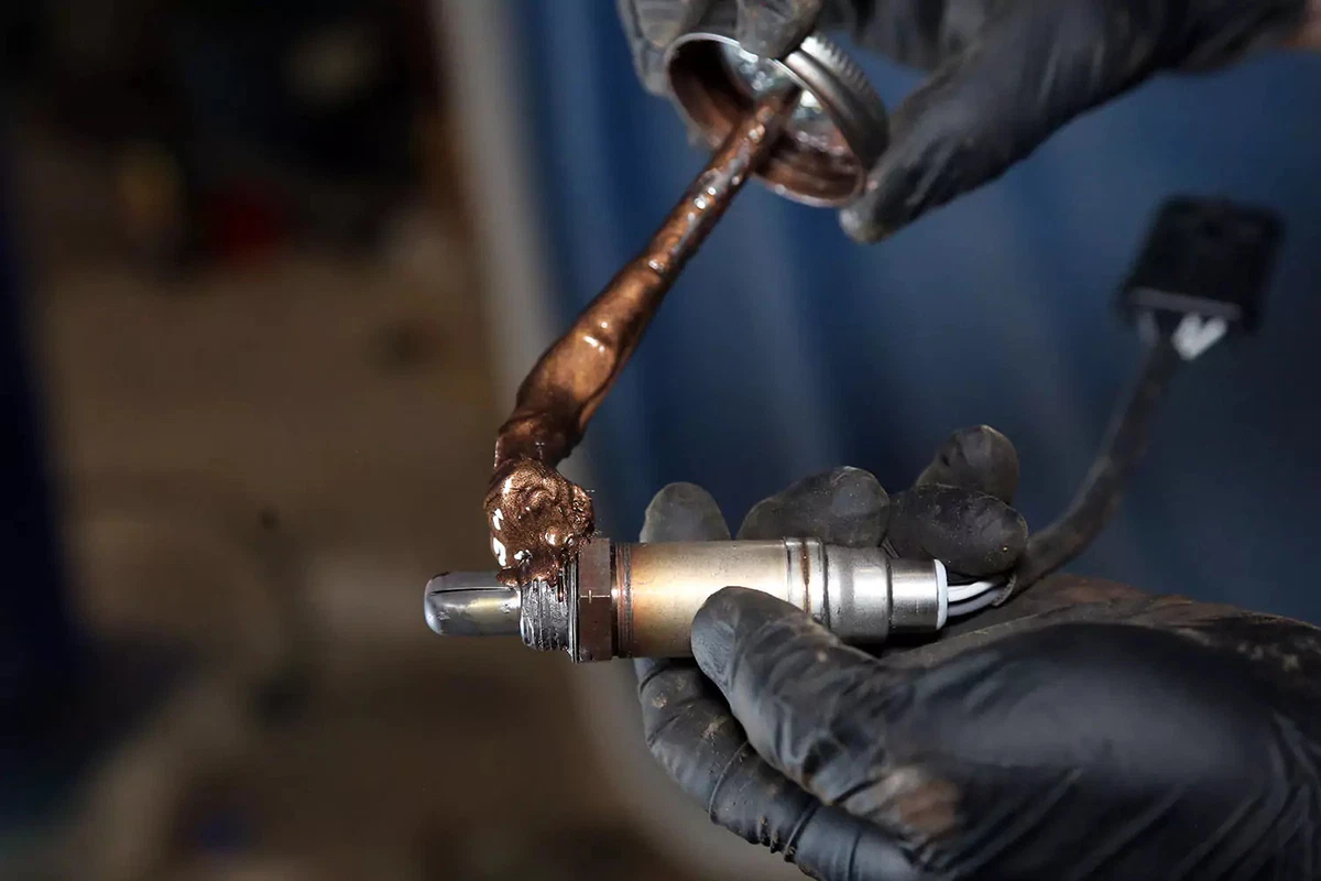 A mechanic coating the new oxygen sensor’s threads with an anti-seize compound.