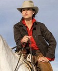 Brown canvas FILSON women’s jacket with red plaid shirt, white hat, and tan leather belt on horseback.