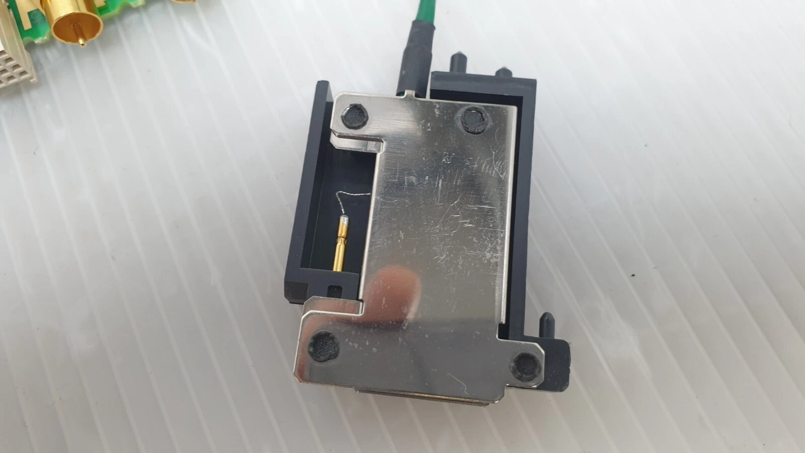 Black connector housing with metal cover and gold contact pin on the green lead