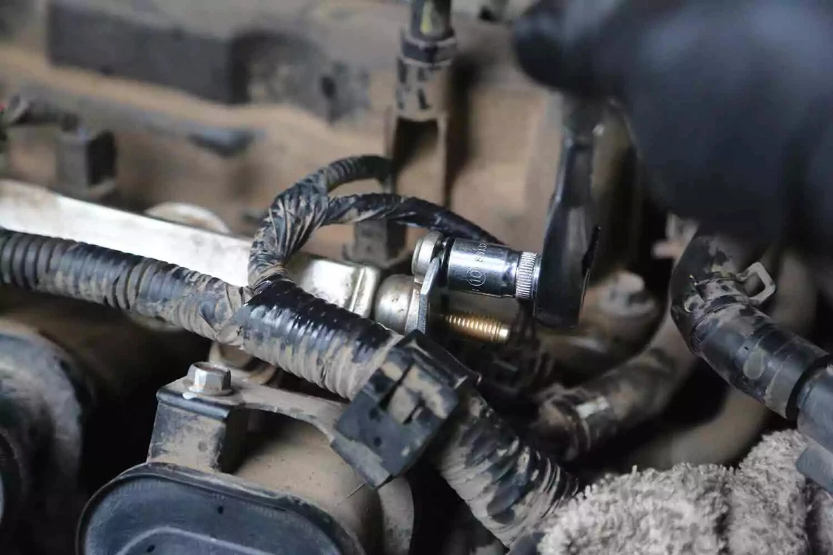 A mechanic uses a socket to tighten the fuel line fitting.