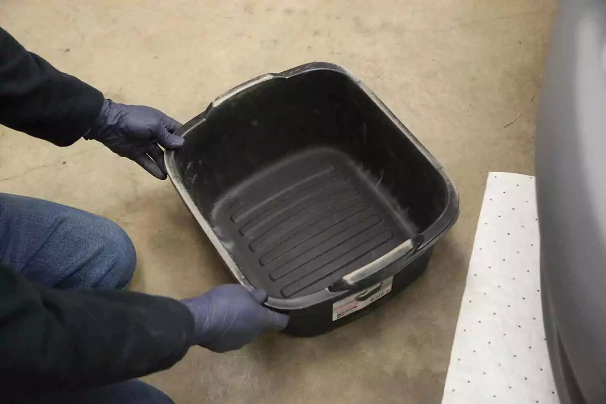 A mechanic wearing blue nitrile gloves slides a drain pan underneath a vehicle’s radiator before draining the coolant.